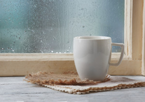 Cup of hot drink with napkin on windowsill on rain background